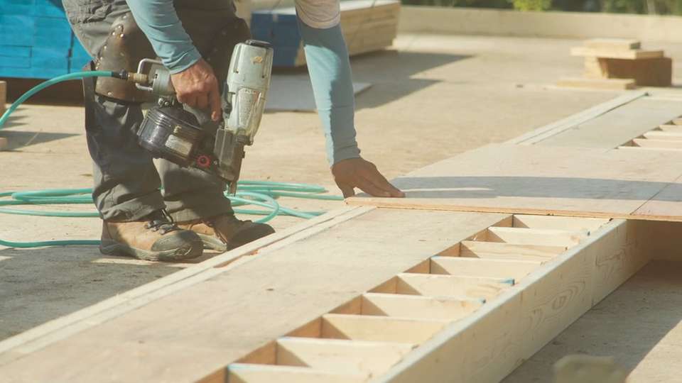 Crew nailing plywood sheathing onto a barn floor frame