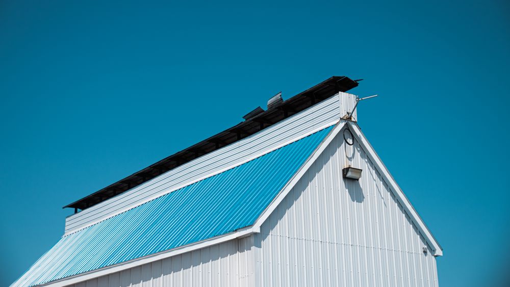 White pole barn with blue metal roof against a clear sky